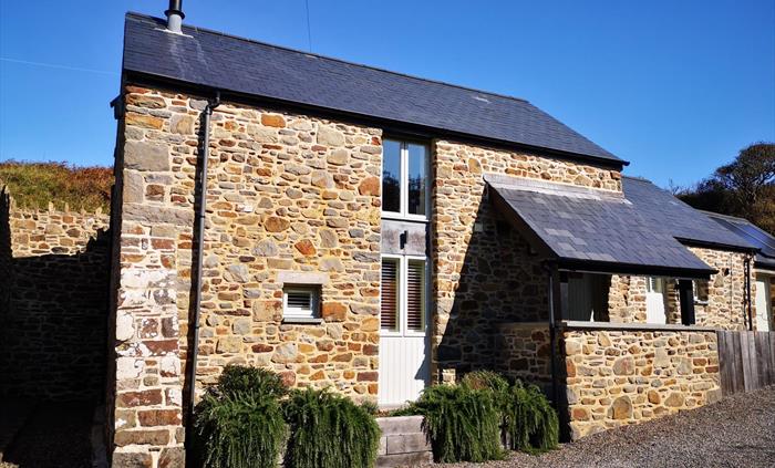 The Mill House seen from the drive on a blue sky day. Slate roof with stone walls.